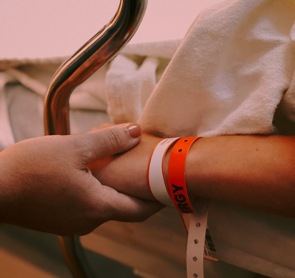 Hand holding patient's hand in hospital bed, by Jon Tyson on Unsplash.